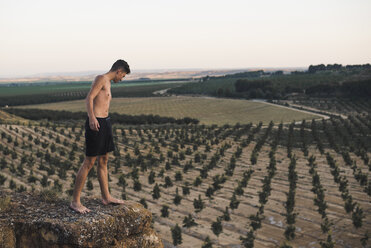 Junger Mann steht auf einem Felsen und blickt auf die Felder - ACPF00143