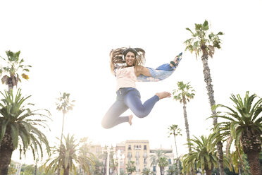 Spain, Barcelona, portrait of smiling young woman with headphones jumping in the air - JNDF00004