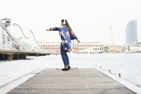Spain, Barcelona, happy young woman with headphones dancing on jetty stock photo