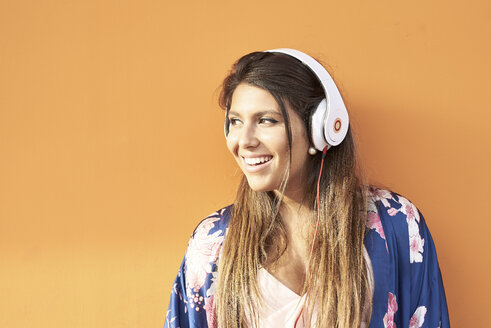 Porträt einer lächelnden jungen Frau mit Kopfhörern vor einem orangefarbenen Hintergrund - JNDF00009