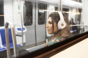 Porträt einer jungen Frau, die in einem U-Bahn-Zug mit Kopfhörern Musik hört - JNDF00017