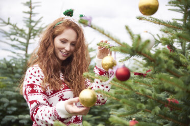 Porträt einer rothaarigen jungen Frau beim Schmücken des Weihnachtsbaums im Freien - ABIF00715