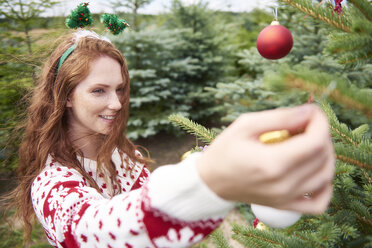 Redheaded young woman decorating Christmas tree outdoors - ABIF00716