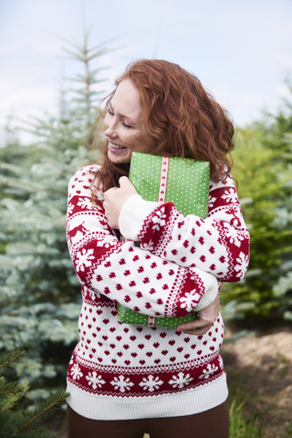 Glückliche rothaarige junge Frau, die ihr Weihnachtsgeschenk im Freien umarmt, lizenzfreies Stockfoto