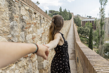 Spanien, Girona, Frau hält die Hand eines Mannes und geht an einer Steinmauer entlang - AFVF00810