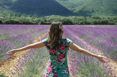 Frankreich, Provence, Valensole-Plateau, Frau steht mit ausgestreckten Armen in Lavendelfeldern im Sommer, lizenzfreies Stockfoto