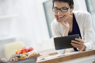 Ein Büro oder eine Wohnung in New York City. Eine Frau in cremefarbener Jacke, die für die Arbeit gekleidet ist, hält eine Tasse Kaffee in der Hand und schaut auf ihr digitales Tablet. - MINF00093