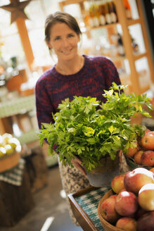 Biobäuerin bei der Arbeit: Eine Frau arbeitet an einem Verkaufsstand mit frischen Produkten, Grünpflanzen und Schalen mit Äpfeln. - MINF00120