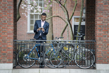 City life in spring. Young people outdoors in a city park. A man in a suit, beside a bicycle park on a sidewalk. Using his smart phone. - MINF00130