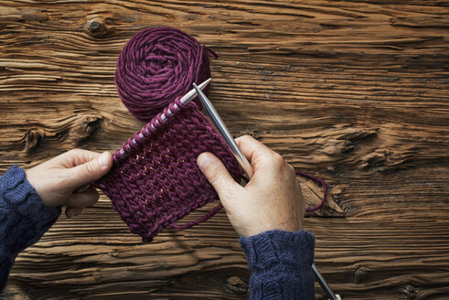 Eine Frau hält zwei Stricknadeln und ein Stück Strickzeug aus lila Wolle in der Hand. - MINF00139