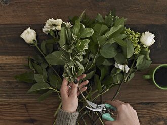 Eine Frau hält eine Gartenschere in der Hand und schneidet die Basis der Blumenstängel für ein Blumenarrangement aus weißen Rosen und grünem Laub ab. - MINF00146