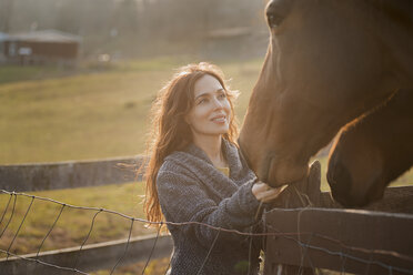 Eine Frau streichelt die Schnauzen von zwei Pferden auf einer Koppel auf einem Biohof. - MINF00164