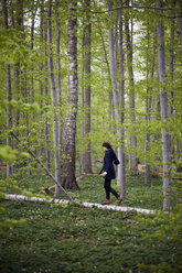 A woman walking along a fallen tree trunk in the woods. Balancing on the narrow piece of wood. - MINF00177