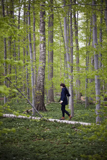 Eine Frau geht im Wald an einem umgestürzten Baumstamm entlang und balanciert auf dem schmalen Stück Holz. - MINF00177