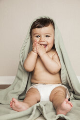 A young 8 month old baby boy wearing cloth diapers, sitting on the floor. A cot blanket over his head. - MINF00186