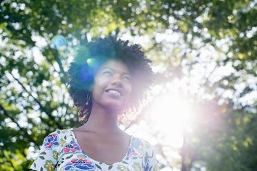 A young woman in a flowered summer dress with her hands behind her head, smiling and looking up. - MINF00189