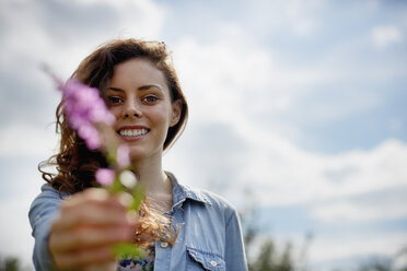 A young woman holding out a wild flower with pink petals. - MINF00197