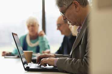 Fokussierter älterer Geschäftsmann mit Laptop in einer Besprechung im Konferenzraum - CAIF21256