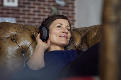 Frau mit Kopfhörer auf dem Sofa liegend, Musik hörend, lizenzfreies Stockfoto