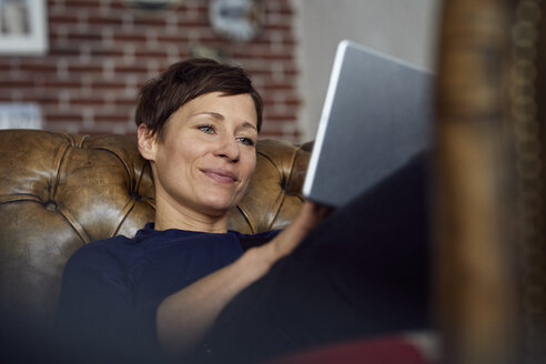 Woamn sitzt zu Hause auf dem Sofa und benutzt ein digitales Tablet - RBF06442