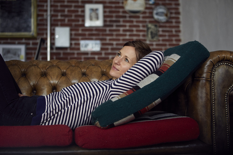 Frau auf dem Sofa, die sich zu Hause entspannt und träumt, lizenzfreies Stockfoto