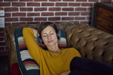 Frau mit Kopfhörer auf dem Sofa liegend, Musik hörend - RBF06449