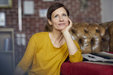 Attraktive Frau sitzt zu Hause mit der Hand am Kinn - RBF06451