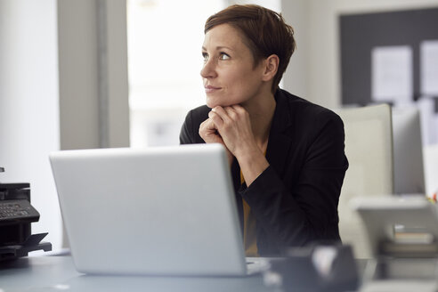 Geschäftsfrau sitzt im Büro und benutzt einen Laptop - RBF06457