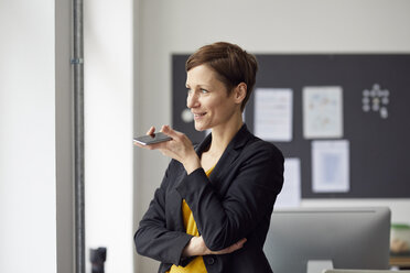 Attraktive Geschäftsfrau, die im Büro steht und ein Smartphone benutzt - RBF06461