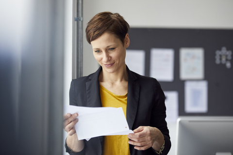 Attraktive Geschäftsfrau steht im Büro und liest ein Dokument, lizenzfreies Stockfoto