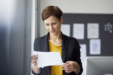 Attraktive Geschäftsfrau steht im Büro und liest ein Dokument - RBF06463