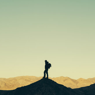 Silhouette eines männlichen Wanderers, der einen Rucksack trägt und auf einer Bergkuppe im Death Valley National Park steht. - MINF00235
