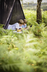 Zwei Jungen zelten im New Forest und liegen unter einem Zeltdach. - MINF00249
