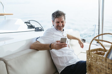 Mature man on a sailing trip having, using smartphone - EBSF02592