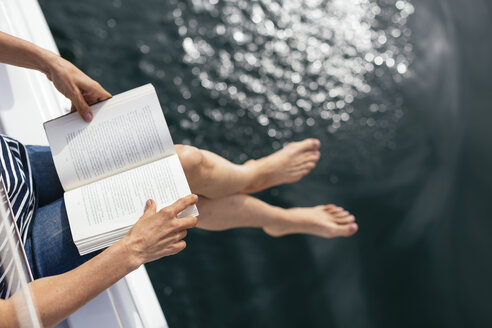 Frau sitzt auf einem Segelboot und liest ein Buch - EBSF02595