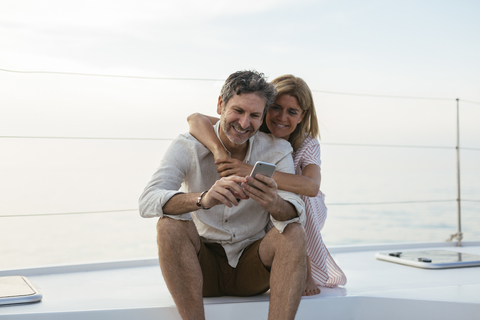 Mature couple looking at smartphone, sitting on a sailing boat stock photo