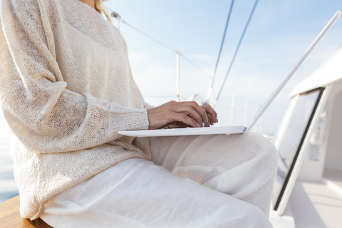 Frau sitzt auf einem Katamaran und benutzt einen Laptop, lizenzfreies Stockfoto