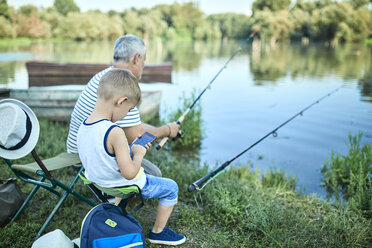 Kleiner Junge sitzt mit seinem Großvater am Seeufer und testet sein Smartphone - ZEDF01477