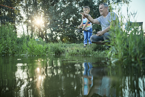 Grandfather and grandson fishing together at lakeshore stock photo