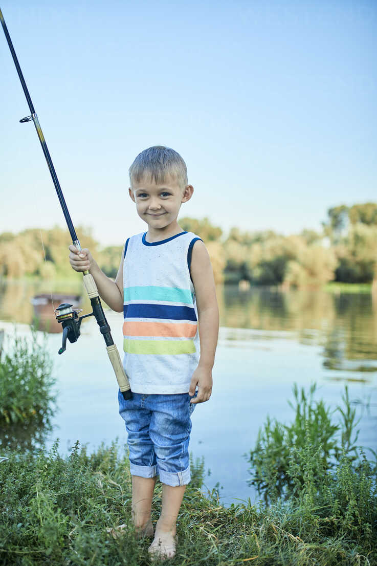 Portrait of smiling little boy with fishing rod at lakeshore stock