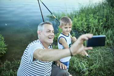 Grandfather and grandson taking selfie with smartphone at lakeshore - ZEDF01491