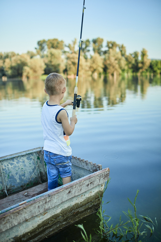 Rückenansicht eines kleinen Jungen mit Angelrute im Boot stehend, lizenzfreies Stockfoto