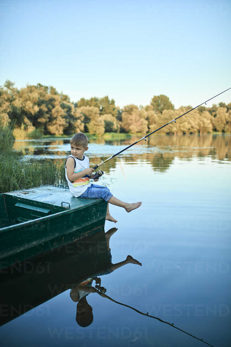 Little boy with fishing rod sitting on boat stock photo