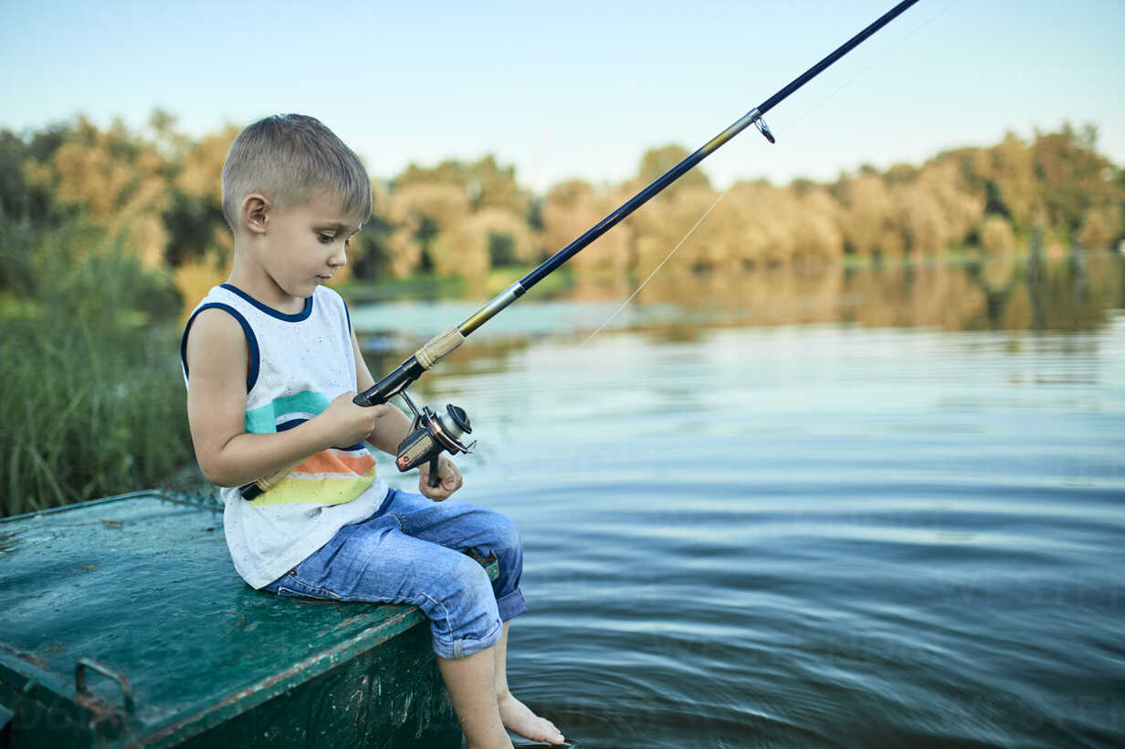 Back view of little boy with fishing rod sitting on boat stock photo