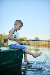 Kleiner Junge mit Angelrute sitzt auf einem Boot und spritzt mit Wasser - ZEDF01496
