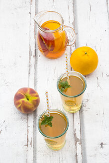 Gläser und Glas mit Pfirsich-Orangen-Eistee auf Holz - LVF07310
