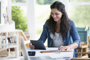 Eine Frau arbeitet an einem Tisch und benutzt ein digitales Tablet. - MINF00289