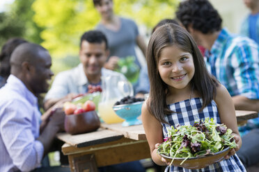 Erwachsene und Kinder an einem Tisch in einem Garten, ein Kind hält eine Schüssel mit Salat. - MINF00292