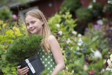 Ein junges Mädchen trägt eine Pflanze in einem Topf. - MINF00310