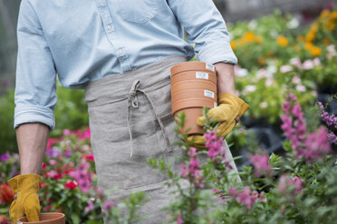 Eine Bio-Gärtnerei, ein Mann trägt Pflanzentöpfe. - MINF00313